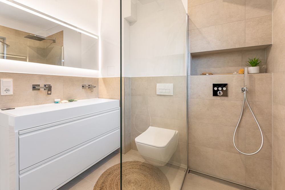 Modernes Badezimmer mit großem Spiegel, weißen Möbeln, WC und begehbarer Dusche.