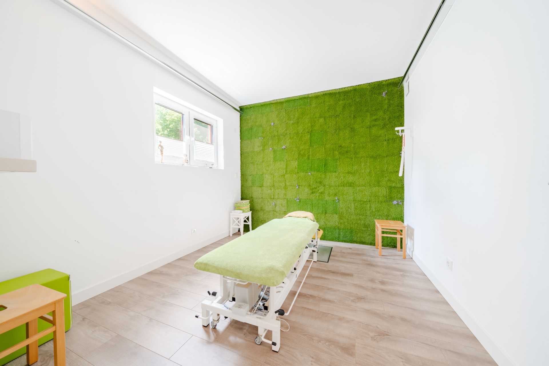Heller Raum mit Massageliege, grüner Wand und Holzfußboden.
