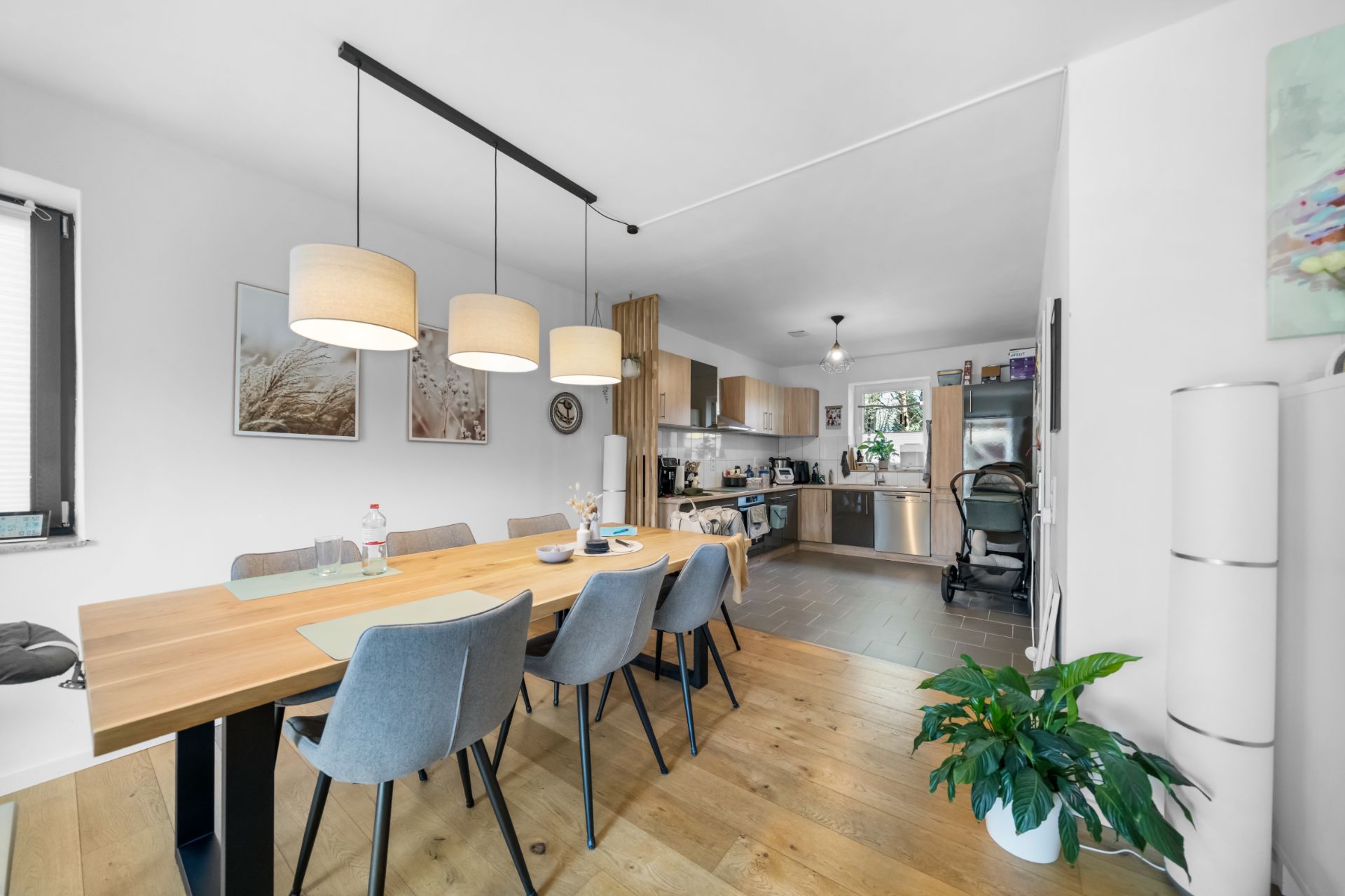 Essbereich mit Holztisch, grauen Stühlen und offener Küche im Hintergrund.