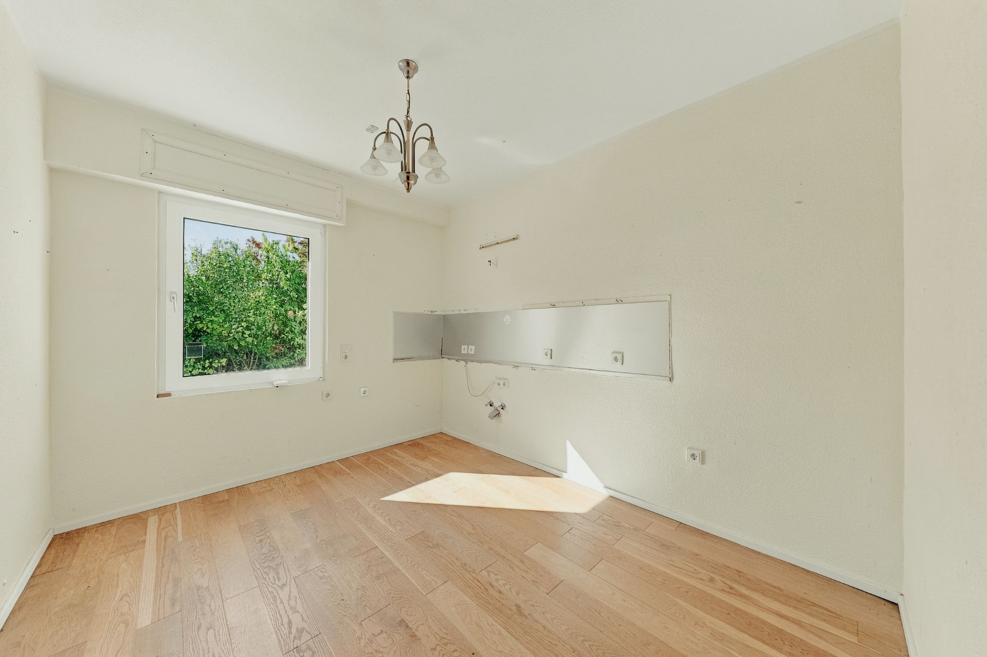 Leerer Raum mit Holzfußboden, weißer Wand, Fenster und Deckenleuchte.
