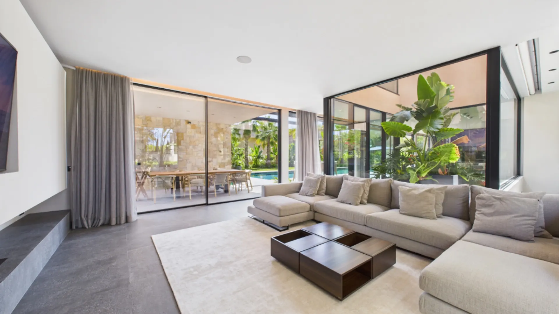 Modernes Wohnzimmer mit großer Ecksofa, Couchtisch und Glasfront mit Blick auf Terrasse und Garten.
