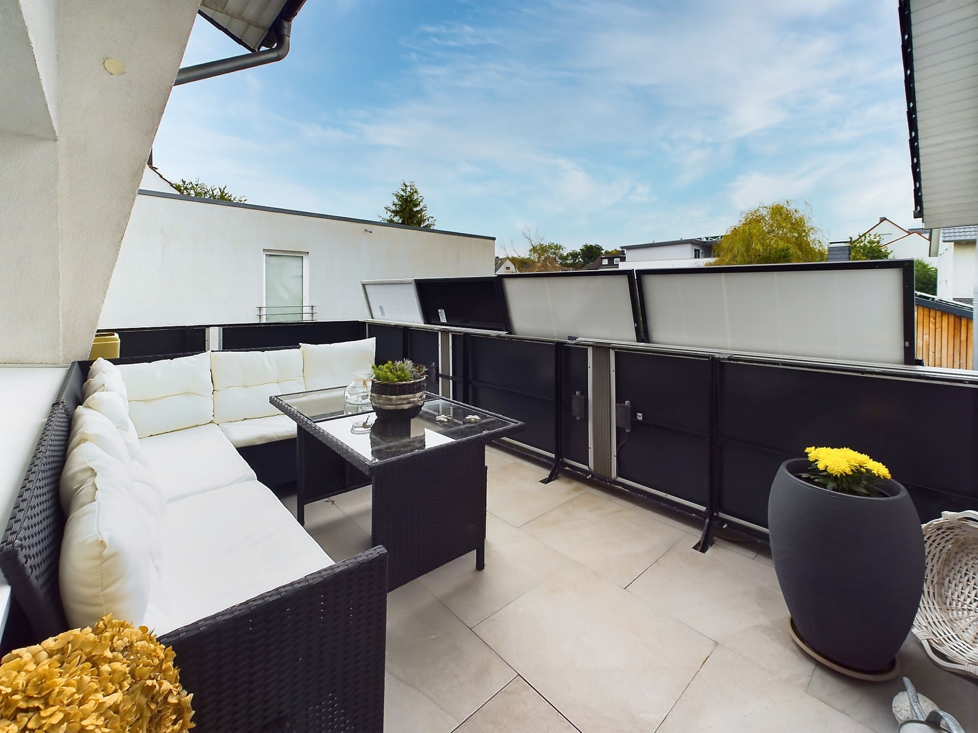 Moderne Terrasse mit weißem Sofa, Glastisch und zwei großen Pflanzkübeln.