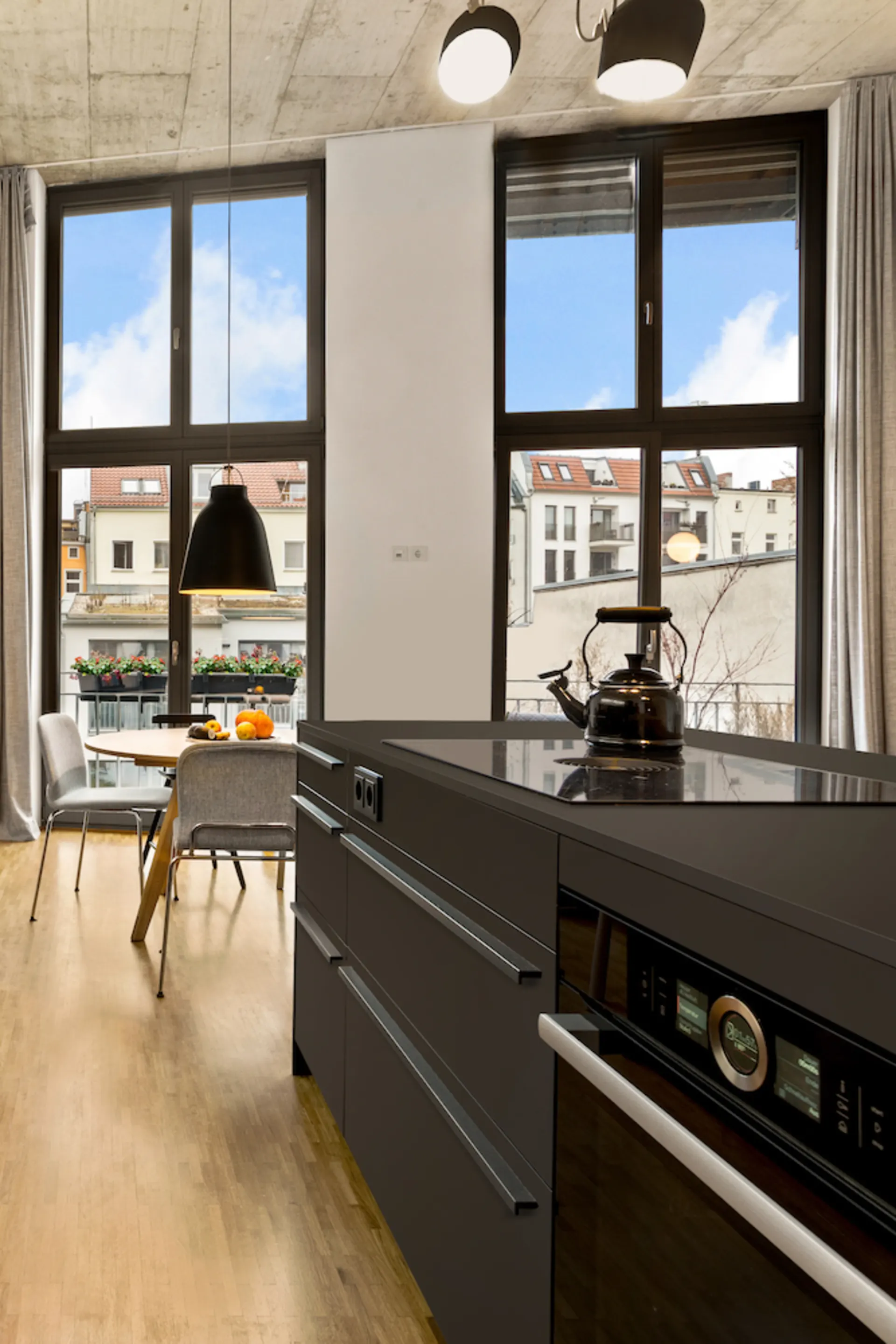 Moderne Küche mit dunkler Kochinsel, großem Fenster und Esstisch im Hintergrund.