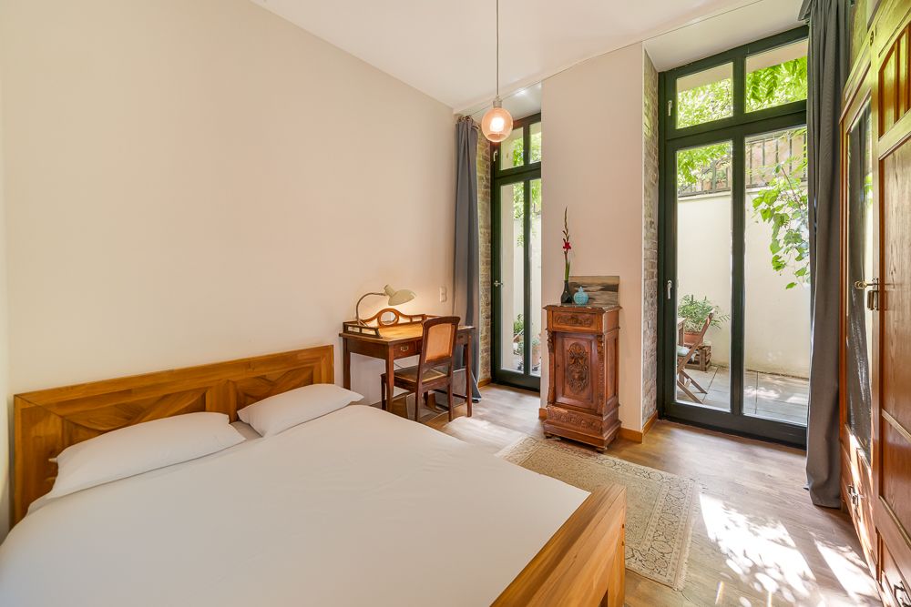 Helles Schlafzimmer mit Holzbett, Schreibtisch und Zugang zu einer Terrasse durch große Glastüren.