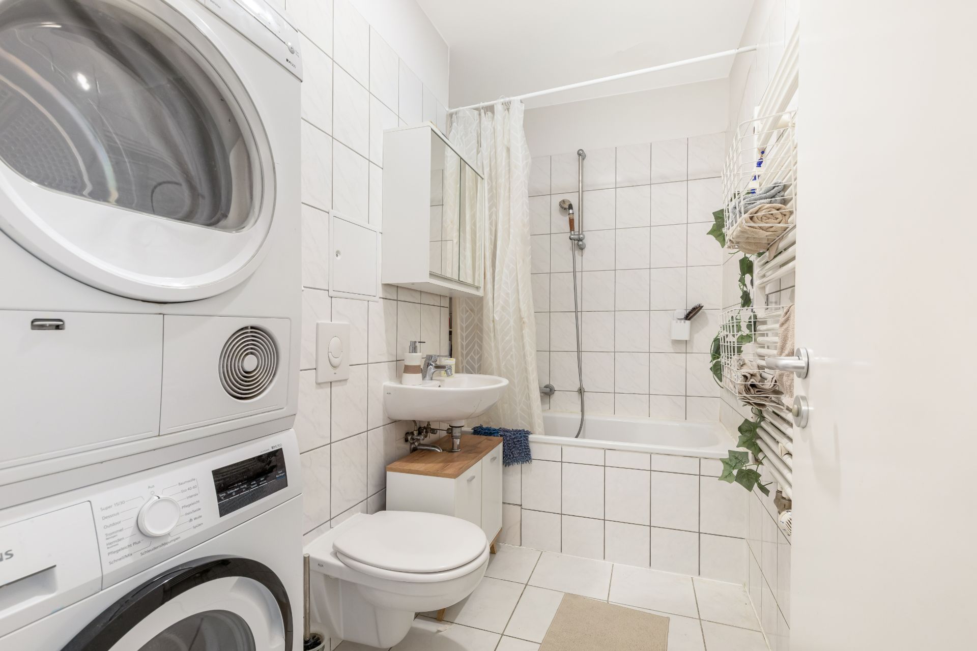 Helles Badezimmer mit Waschmaschine und Trockner, Badewanne, Waschbecken und Toilette.