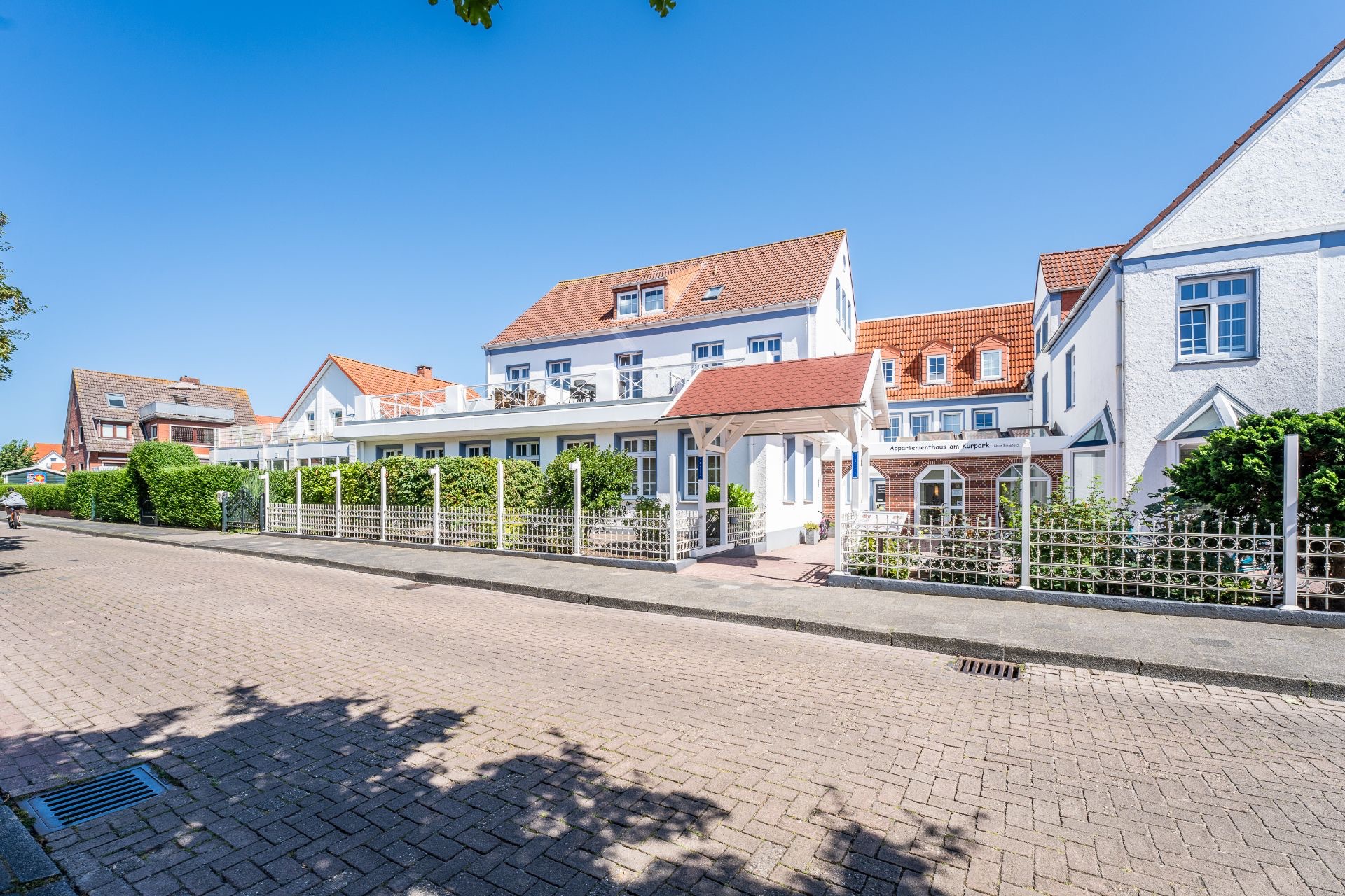 Weiße Wohnhäuser mit roten Dächern und Vorgarten an einer ruhigen Straße.