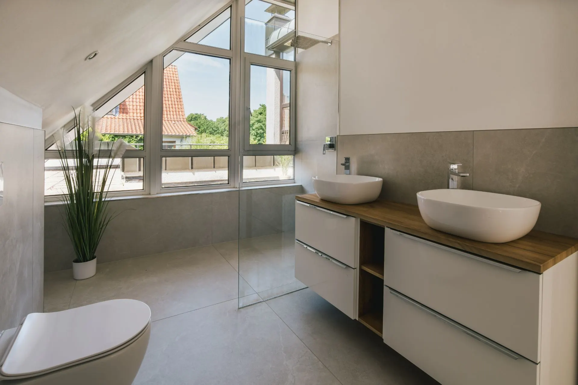 Modernes Badezimmer mit zwei Waschbecken, Toilette, bodentiefem Fenster und Zimmerpflanze.
