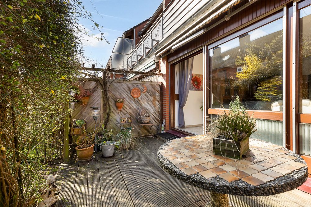 Kleine Terrasse mit runder Tischplatte, Pflanzen, Holzsichtschutz und Zugang ins Wohnzimmer.