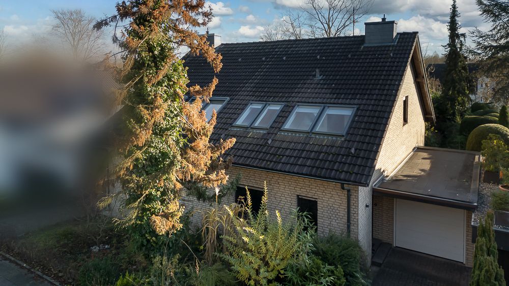 Einfamilienhaus mit dunklem Dach, vielen Fenstern und Garage, umgeben von Bäumen und Pflanzen.