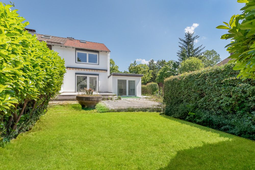 Blick auf einen Garten mit Rasenfläche und Terrasse hinter einem weißen Wohnhaus.