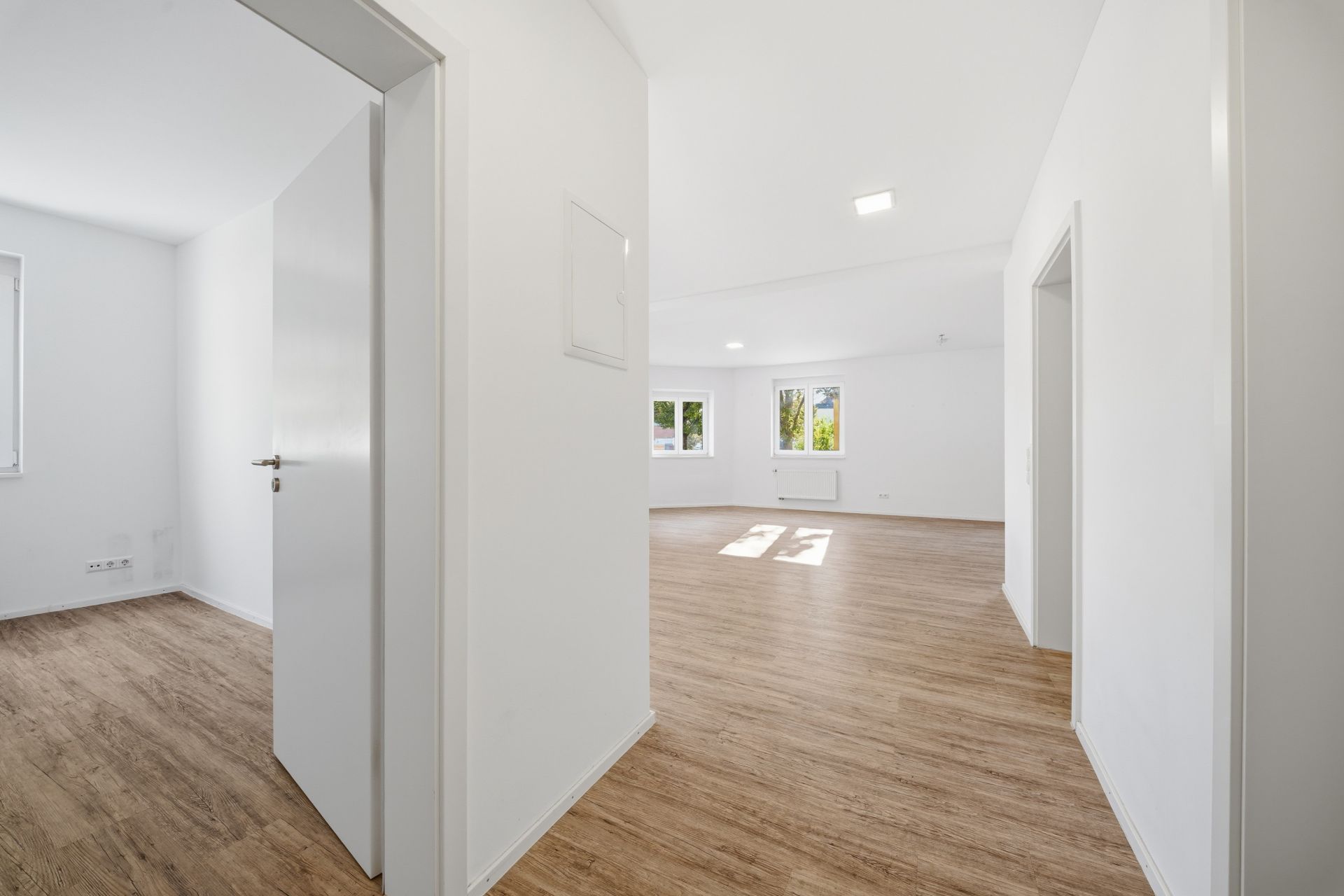 Heller Flur mit Holzboden, Blick in zwei Zimmer mit weißen Wänden und Fenstern.
