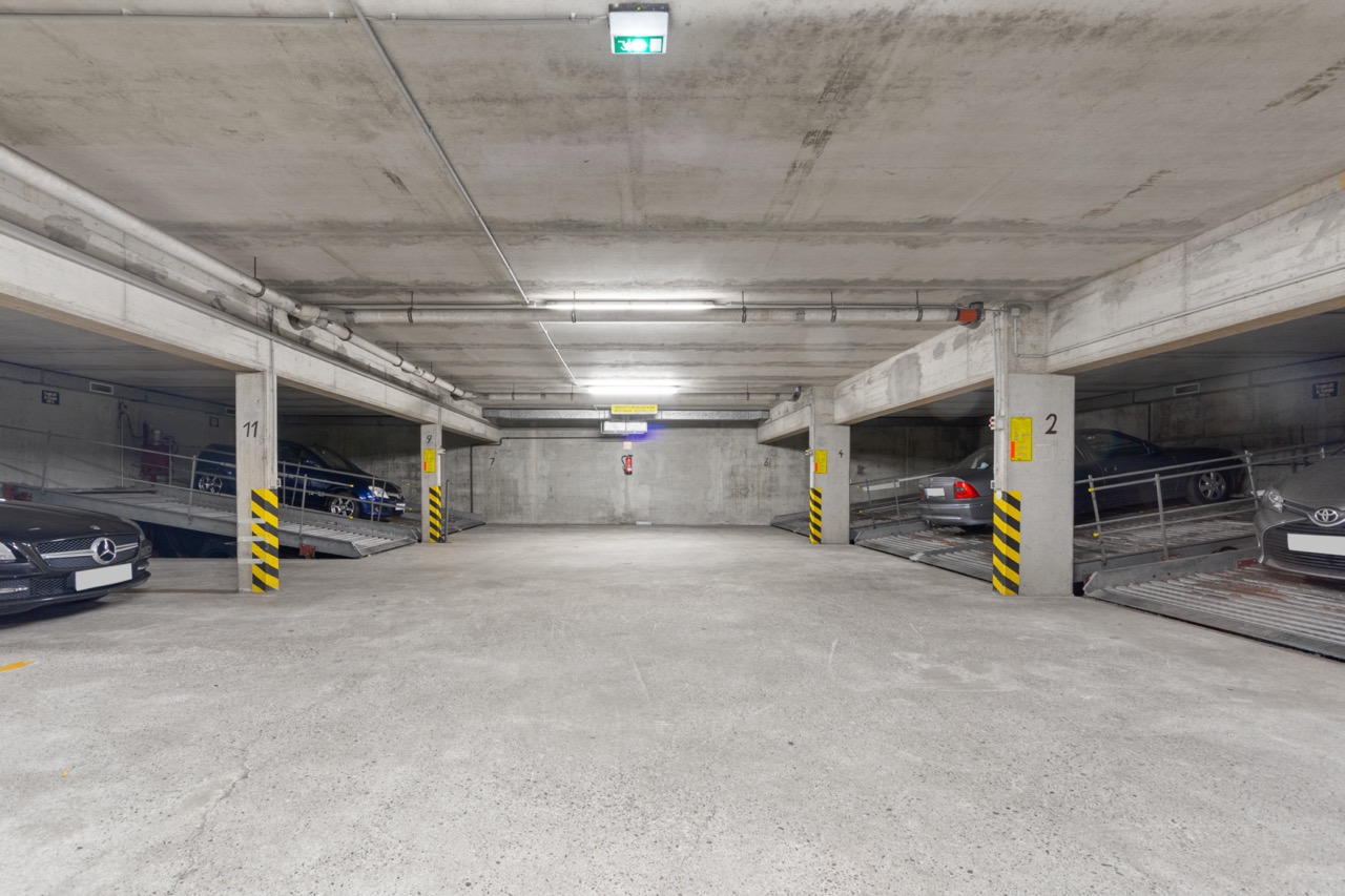 Tiefgarage mit mehreren geparkten Autos und Betonpfeilern mit gelb-schwarzen Markierungen.