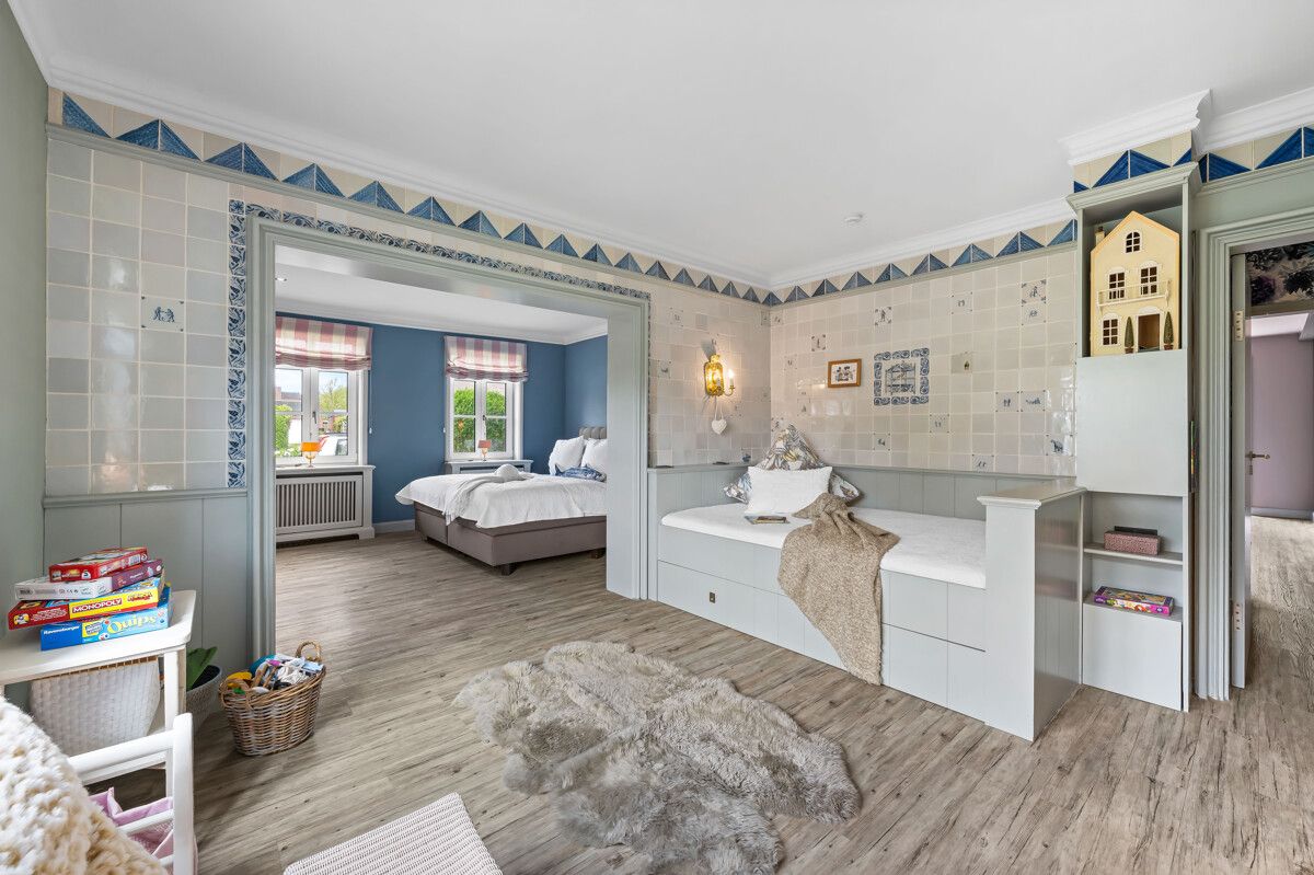 Helles Kinderzimmer mit Spielteppich, Spielzeug und Zugang zu einem Schlafzimmer mit Doppelbett.