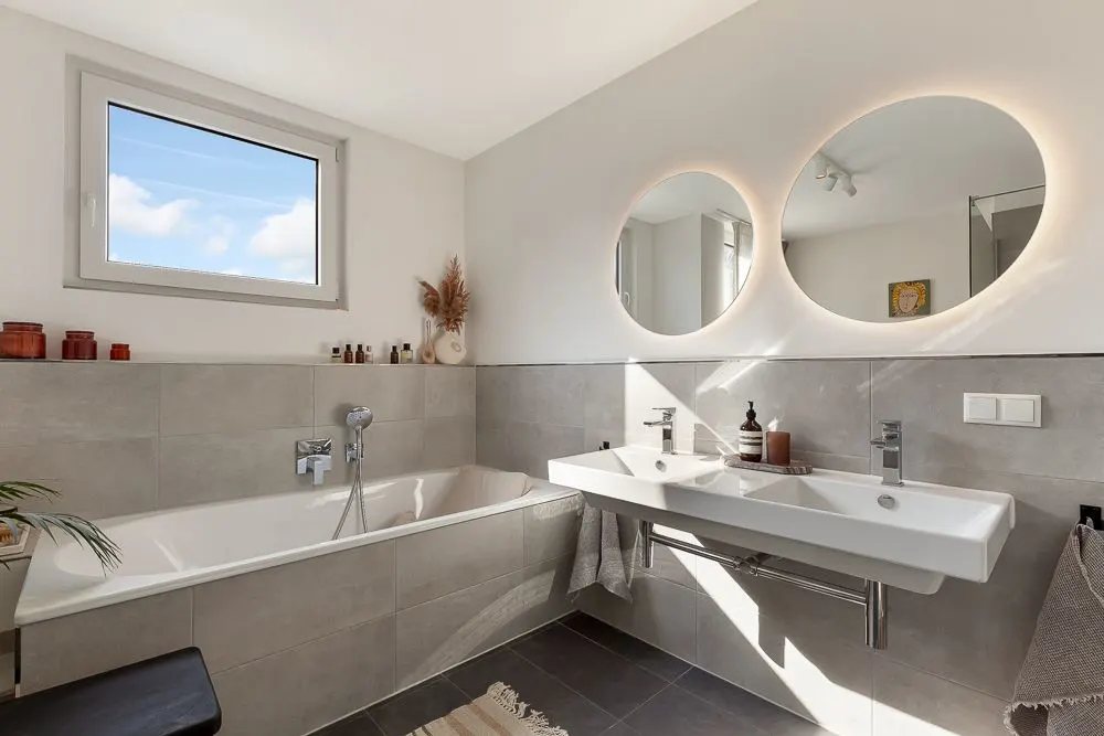 Modernes Badezimmer mit Badewanne, Doppelwaschbecken und beleuchteten Spiegeln.