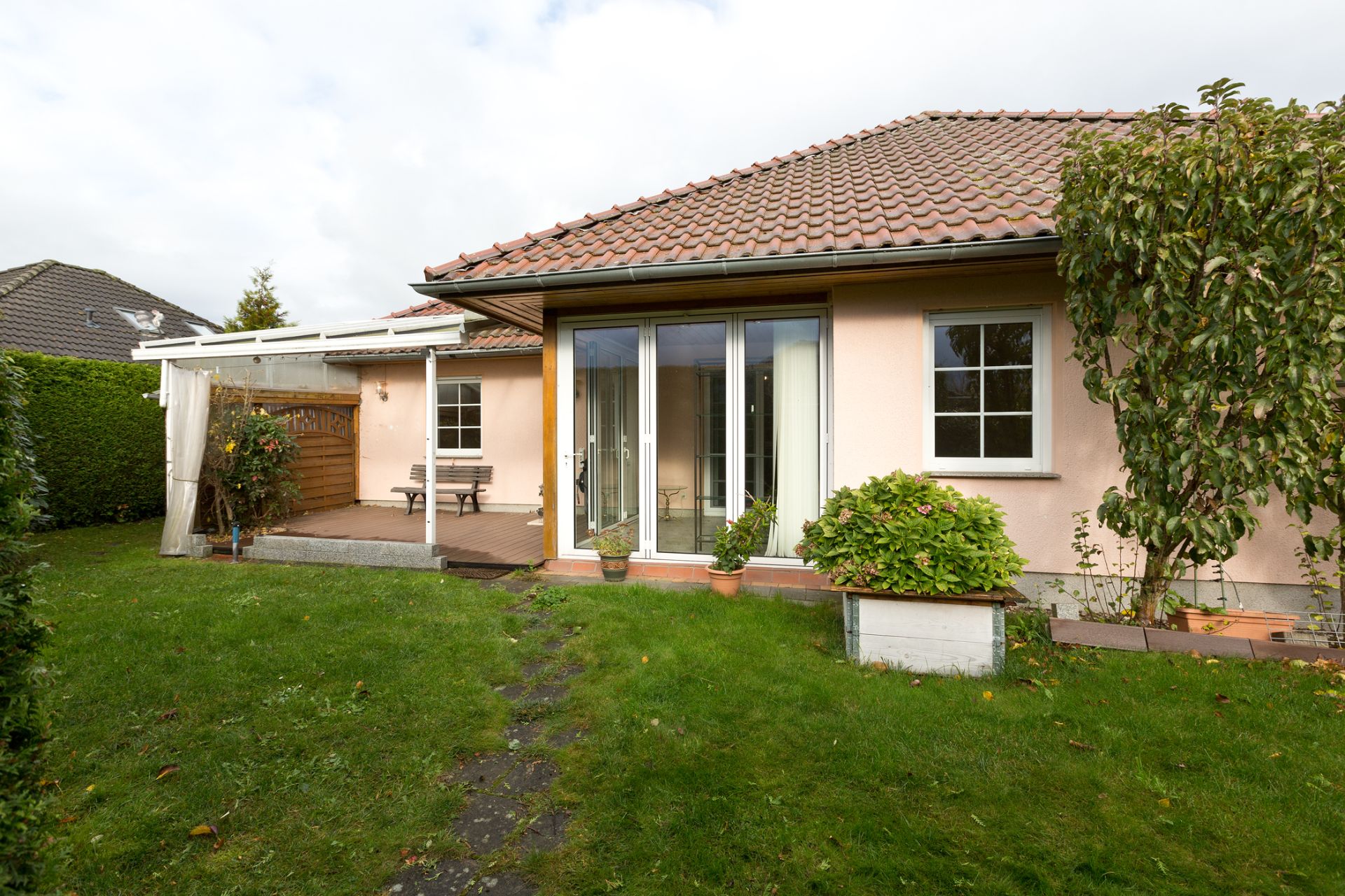 Einfamilienhaus mit Glas-Schiebetür, kleinem Garten und überdachter Terrasse.