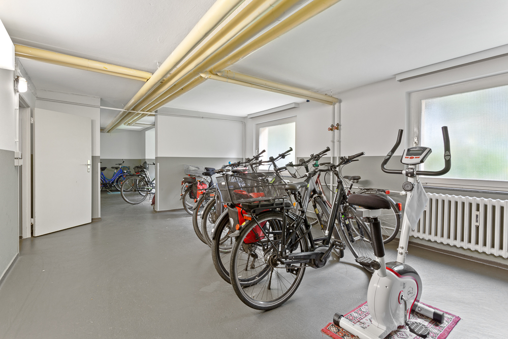 Fahrradraum mit mehreren Fahrrädern und einem Heimtrainer, helle Fenster und offene Tür.