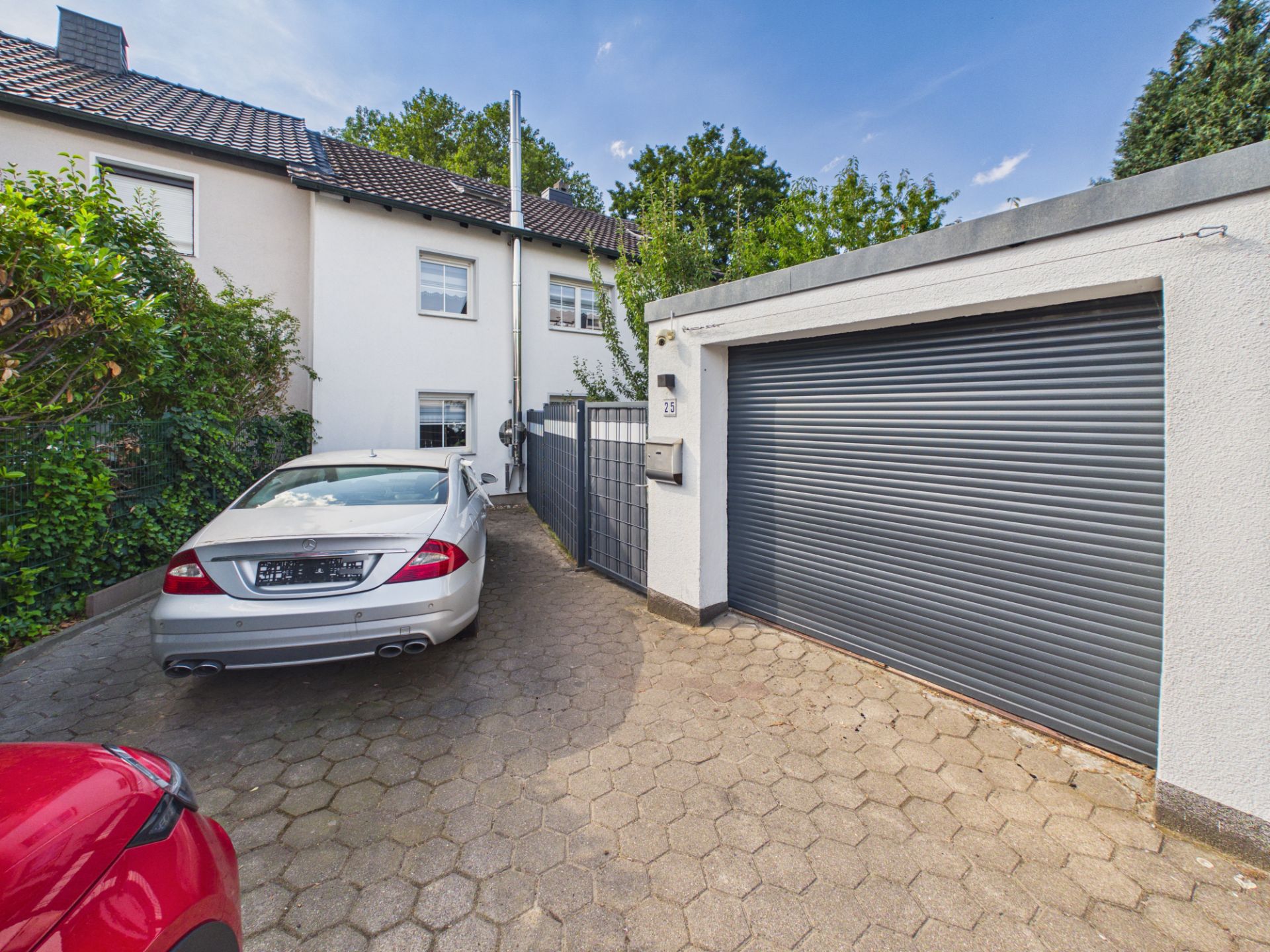 Zufahrt mit zwei geparkten Autos, Garage mit Rolltor und weißes Wohnhaus im Hintergrund.