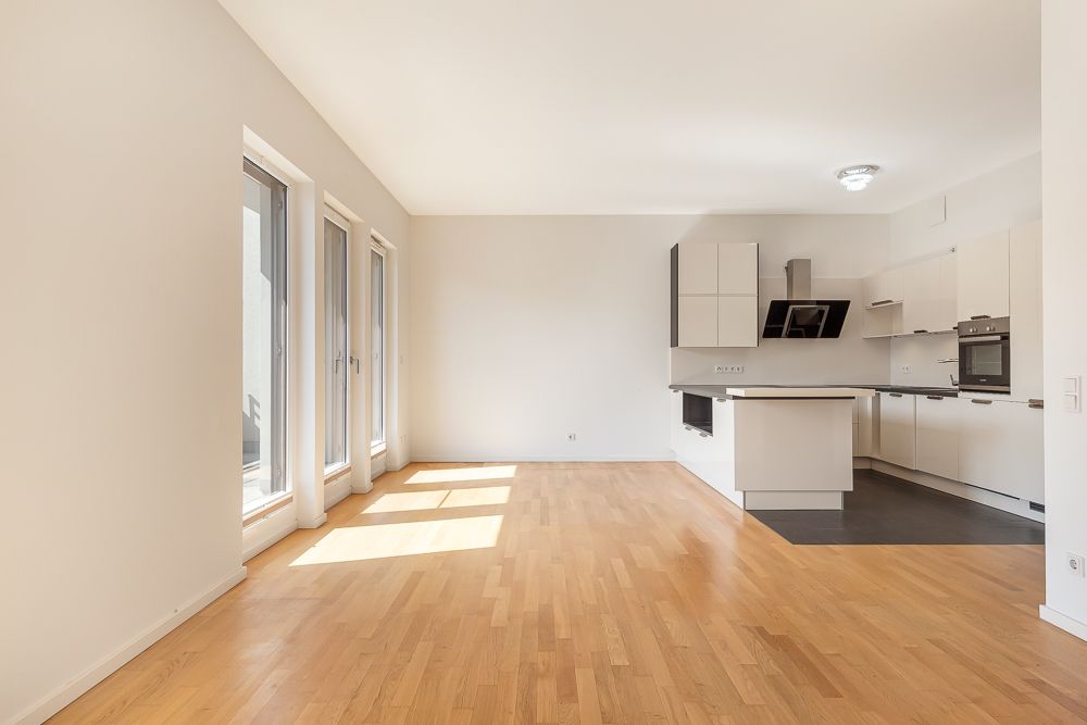 Heller Wohnraum mit Holzboden, großen Fenstern und offener Küche.