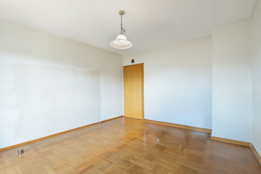 Leerer Raum mit Parkettboden, weiß gestrichenen Wänden und Holztür.