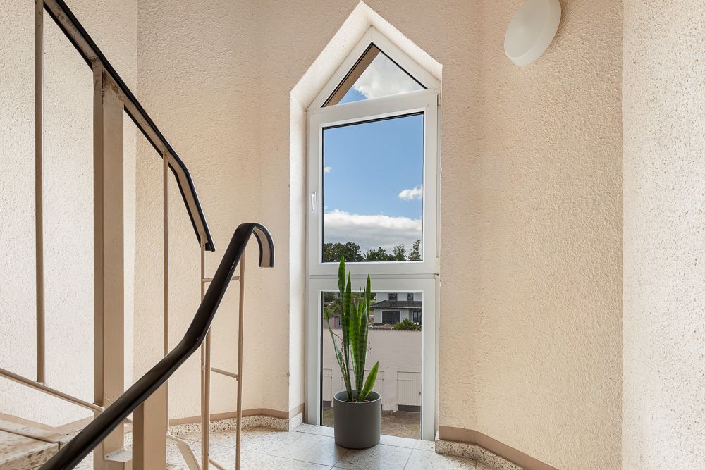 Treppenhaus mit Fenster, Handlauf und einer Pflanze im Topf vor dem Fenster.