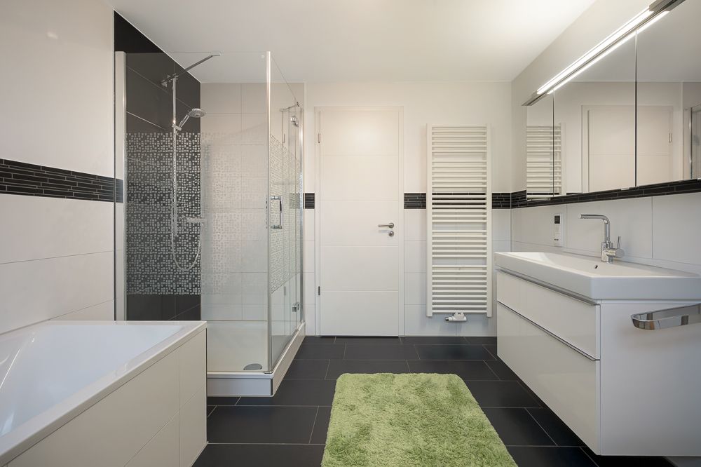Modernes Bad mit Dusche, Badewanne, Waschbecken, grünem Teppich und Handtuchheizkörper.