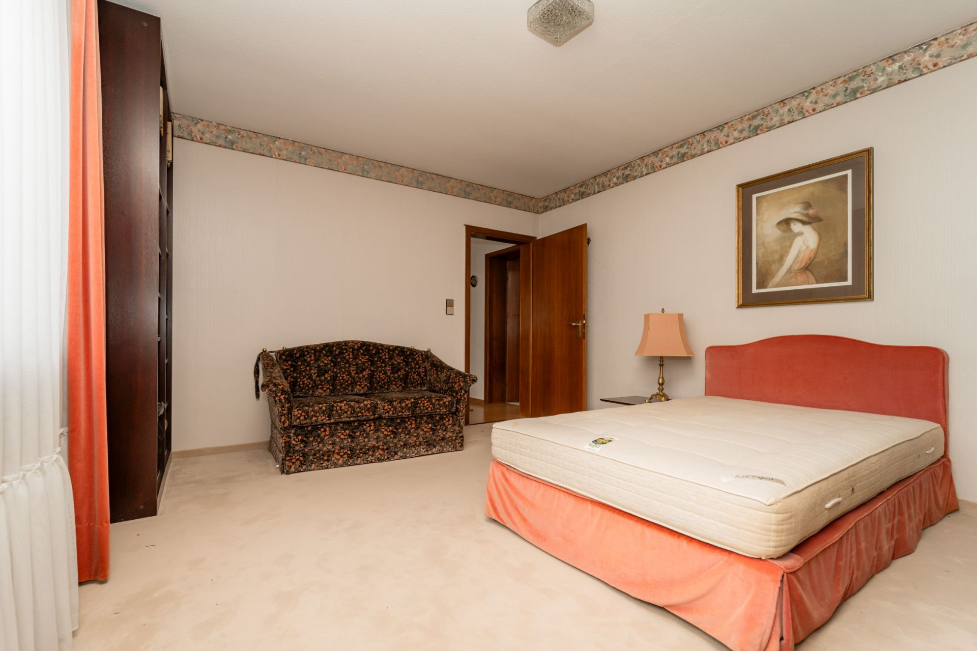 Schlafzimmer mit rotem Bett, Nachttischlampe, Sofa und Wandbild.
