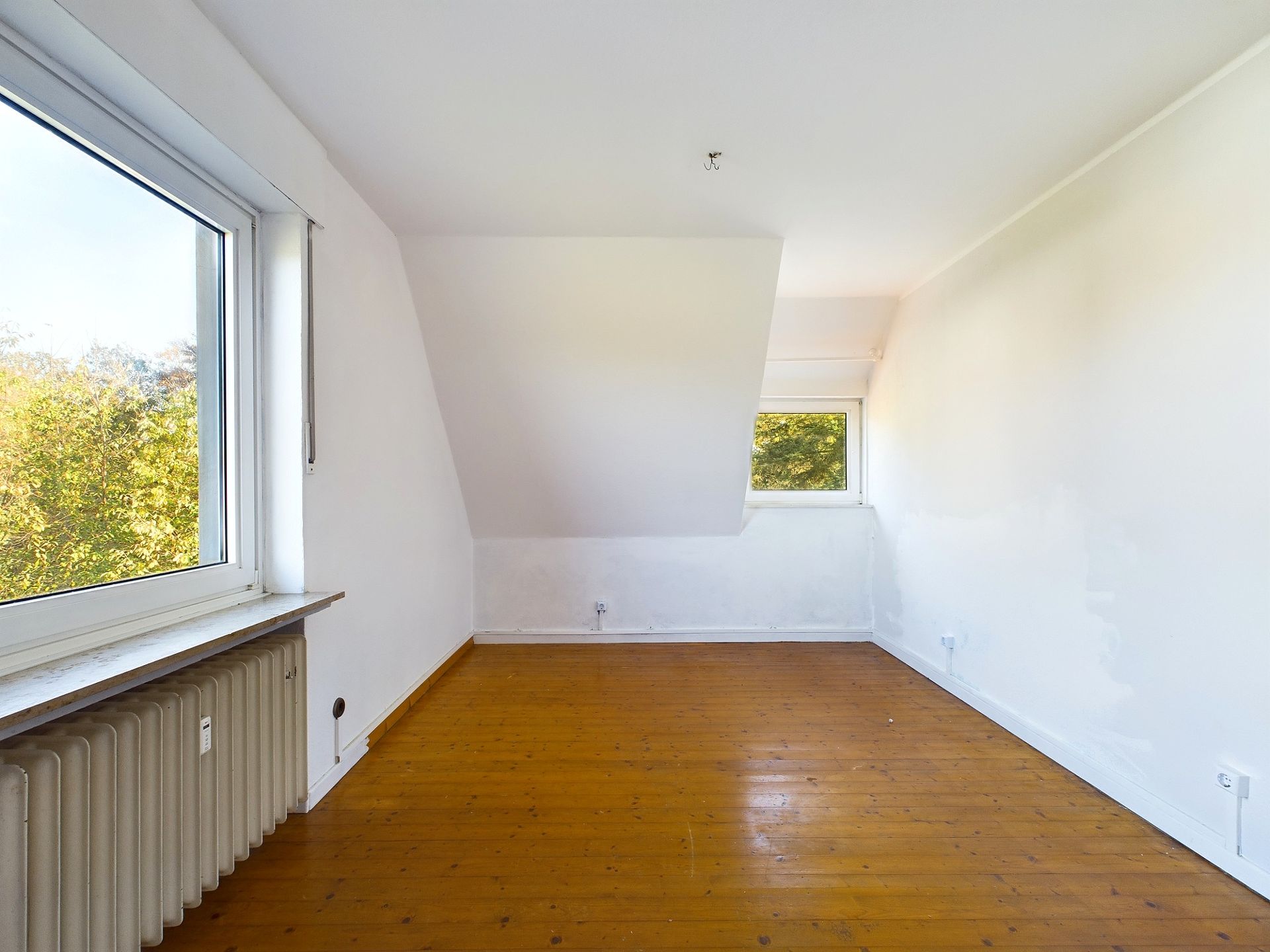 Leerer Raum mit weiß gestrichenen Wänden, Holzfußboden und zwei Fenstern.