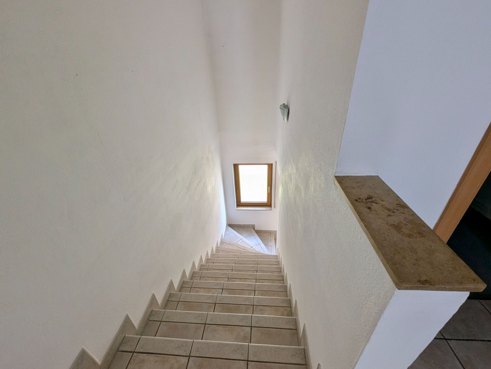 Geflieste Treppe mit weißer Wand und Fenster am Ende.
