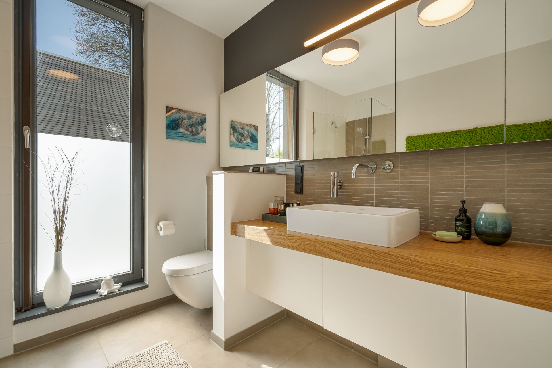 Modernes Badezimmer mit großem Fenster, Waschbecken, Spiegel und Holzablage.