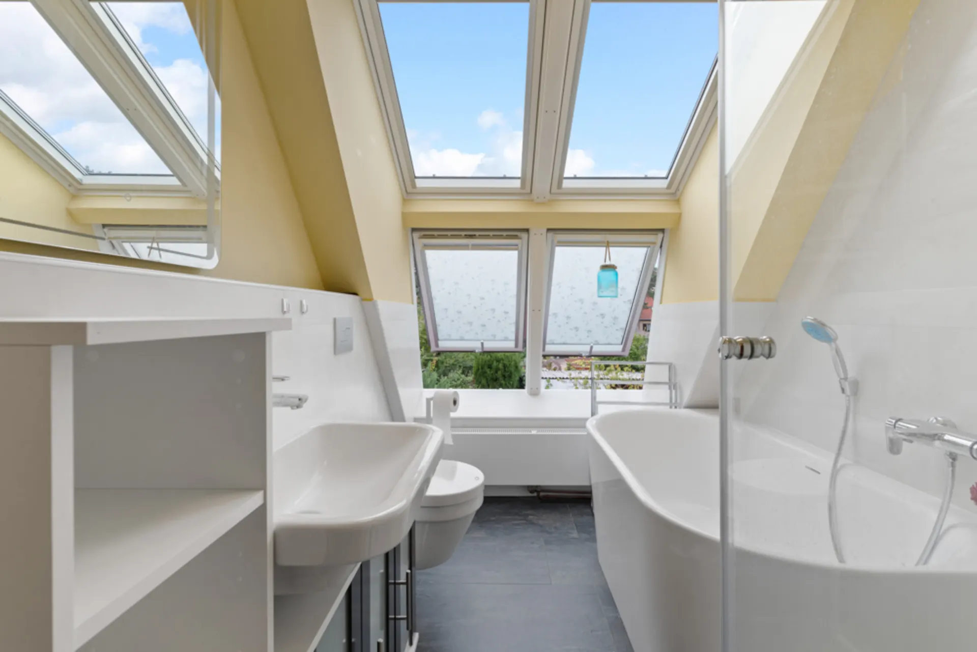 Modernes Badezimmer mit Badewanne, Waschbecken und großen Dachfenstern unter einer Dachschräge.
