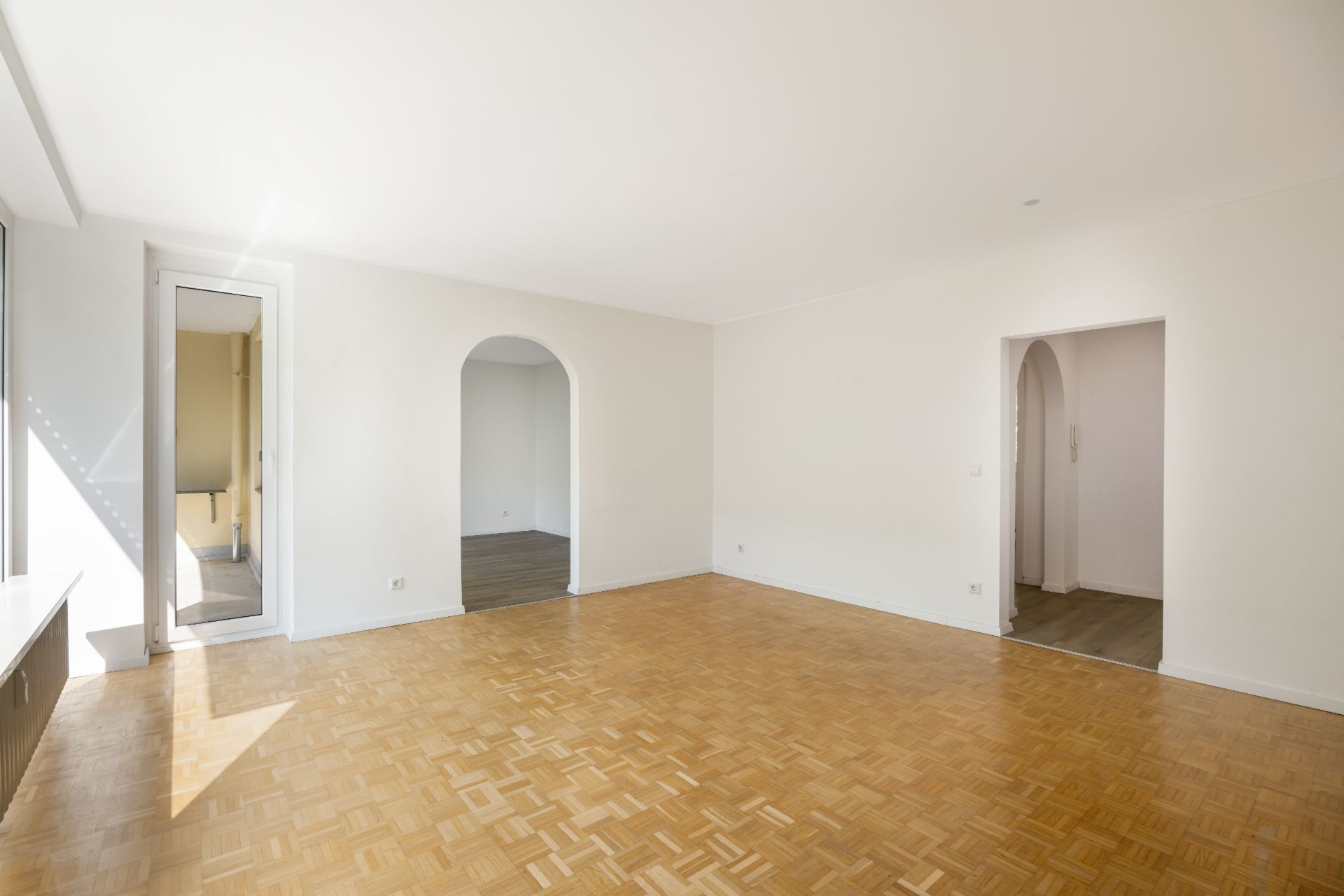 Helles leeres Zimmer mit Parkettboden, weißen Wänden und zwei Durchgängen.