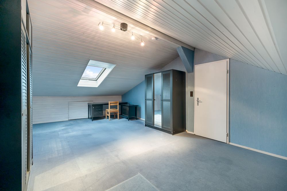 Geräumiges Dachzimmer mit Dachfenster, Schrank, Schreibtisch und Stuhl, blauem Teppich und weißer Tür.