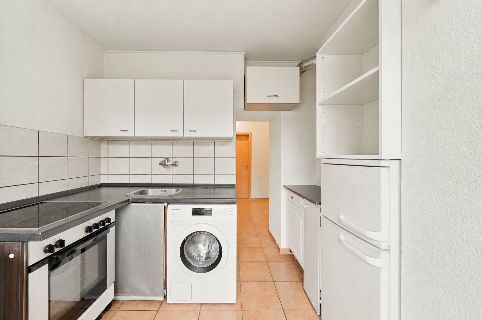 Helle Einbauküche mit Herd, Waschmaschine, Kühlschrank und weißen Schränken.