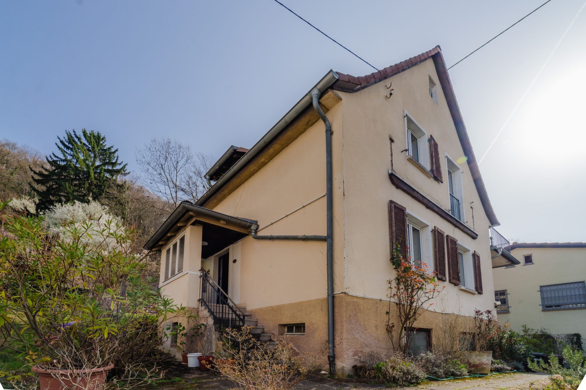 Zweistöckiges Haus mit überdachtem Eingang, braunen Fensterläden und kleinem Garten.