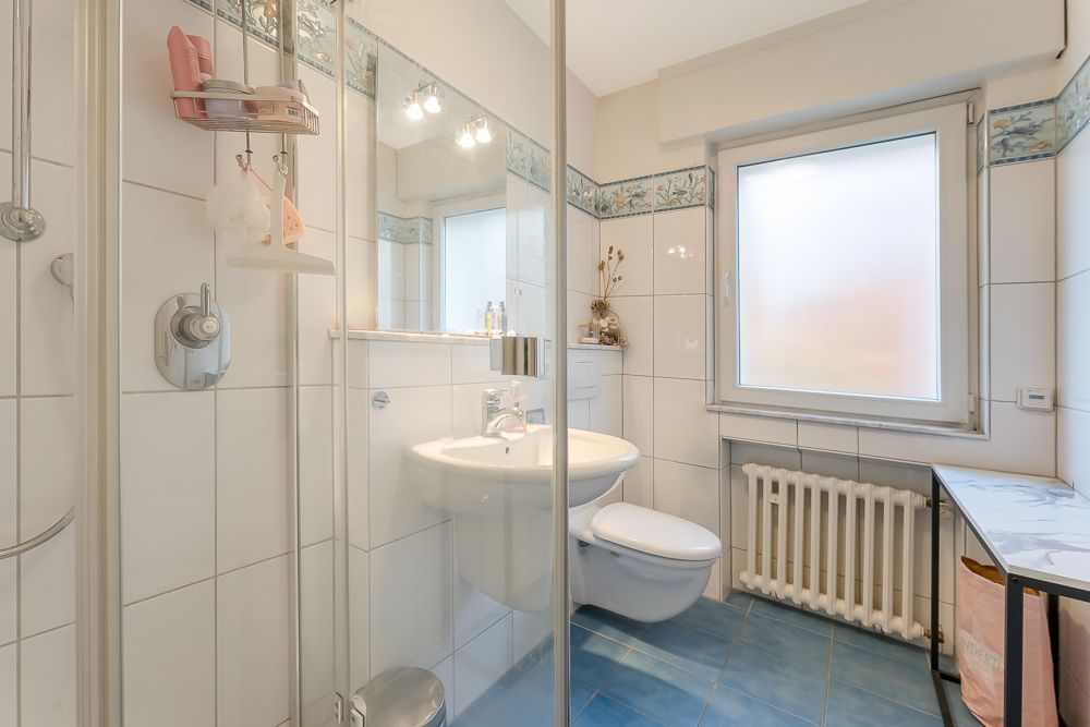 Helles Badezimmer mit Dusche, Waschbecken, WC, Fenster und blauem Fliesenboden.