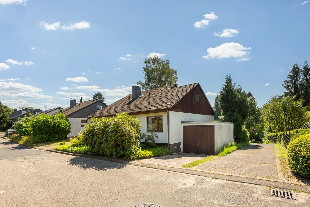 Einfamilienhaus mit Garage und Garten an einer ruhigen Wohnstraße bei Sonnenschein.