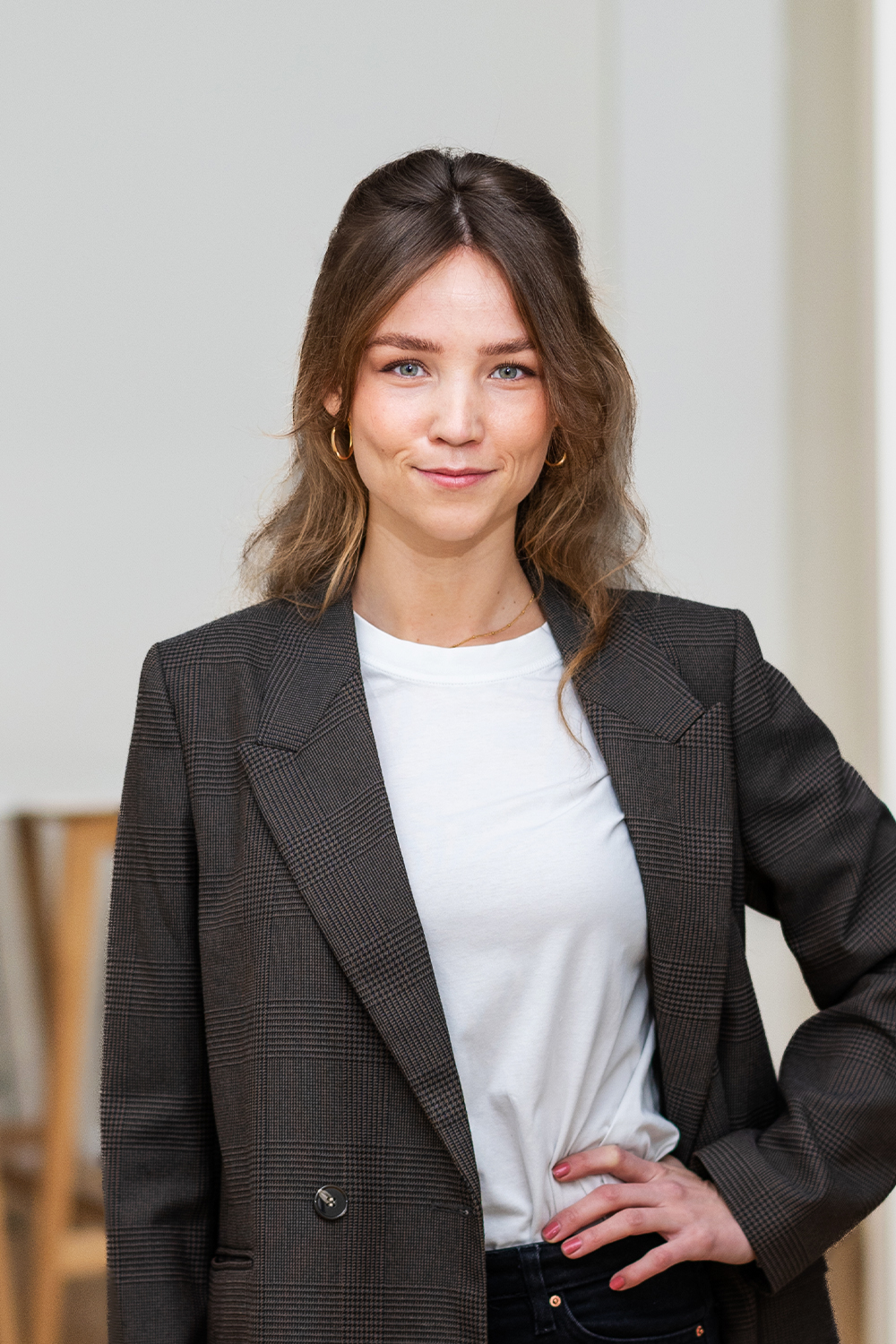 Junge Frau mit langem Haar und kariertem Blazer steht in einem hellen Raum.