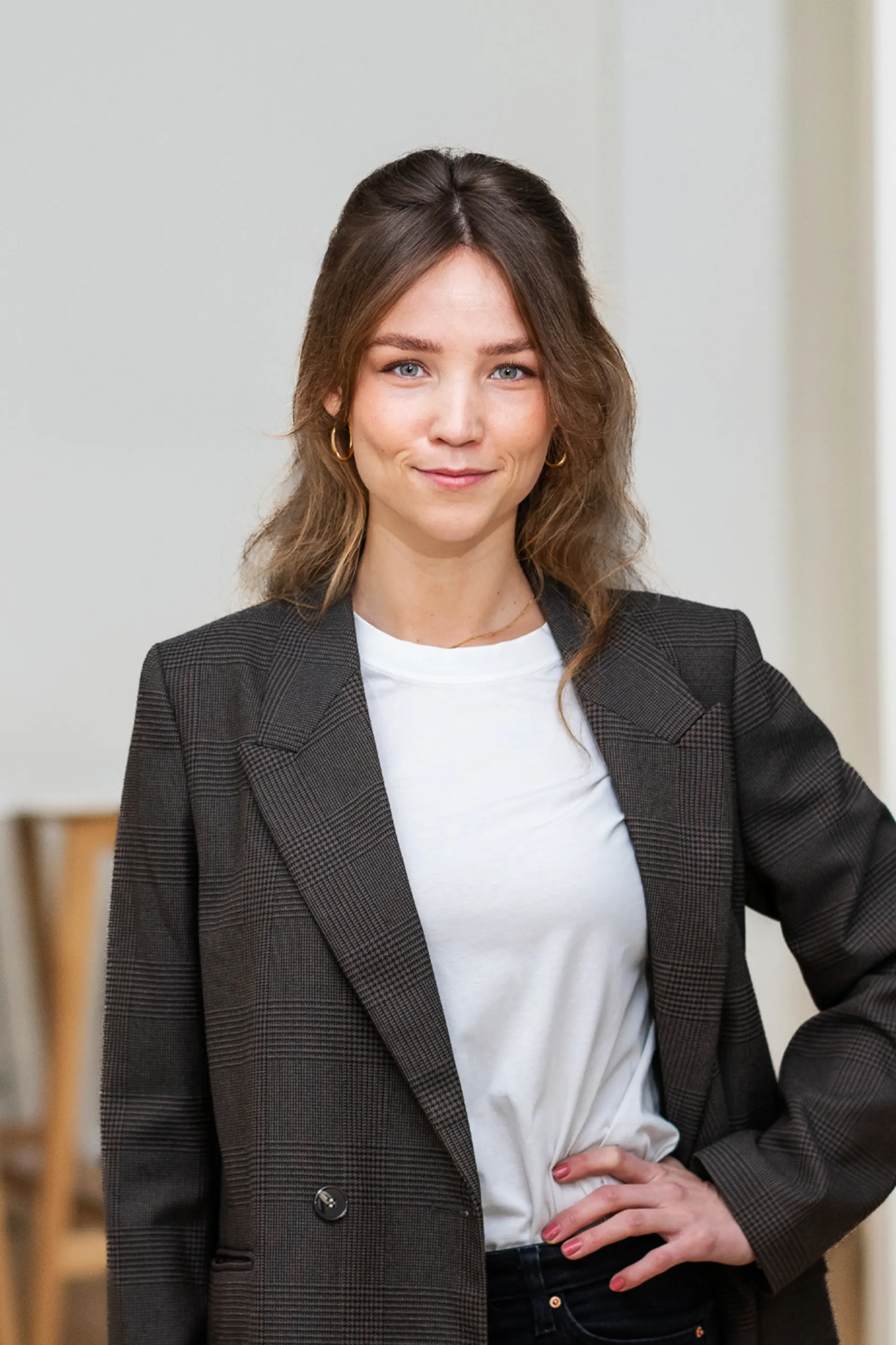 Junge Frau mit langem Haar und kariertem Blazer steht in einem hellen Raum.