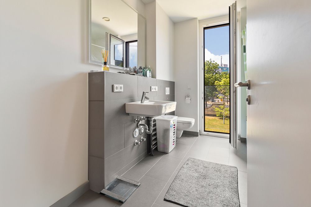 Modernes Badezimmer mit Waschbecken, Spiegel, WC und offener Tür zum Balkon.