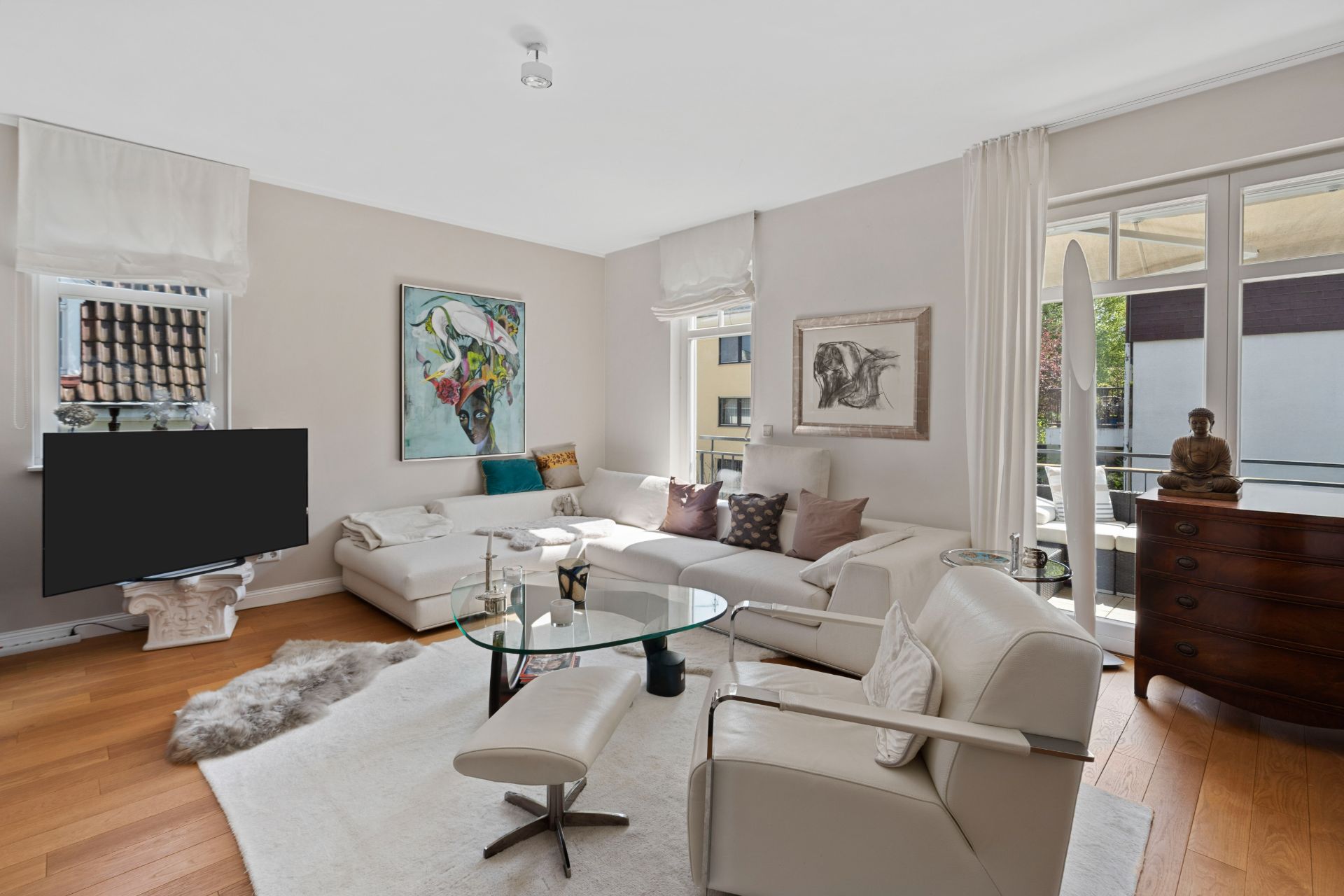 Helles Wohnzimmer mit weißen Möbeln, großem Fenster, Fernseher und Dekoration auf Parkettboden.