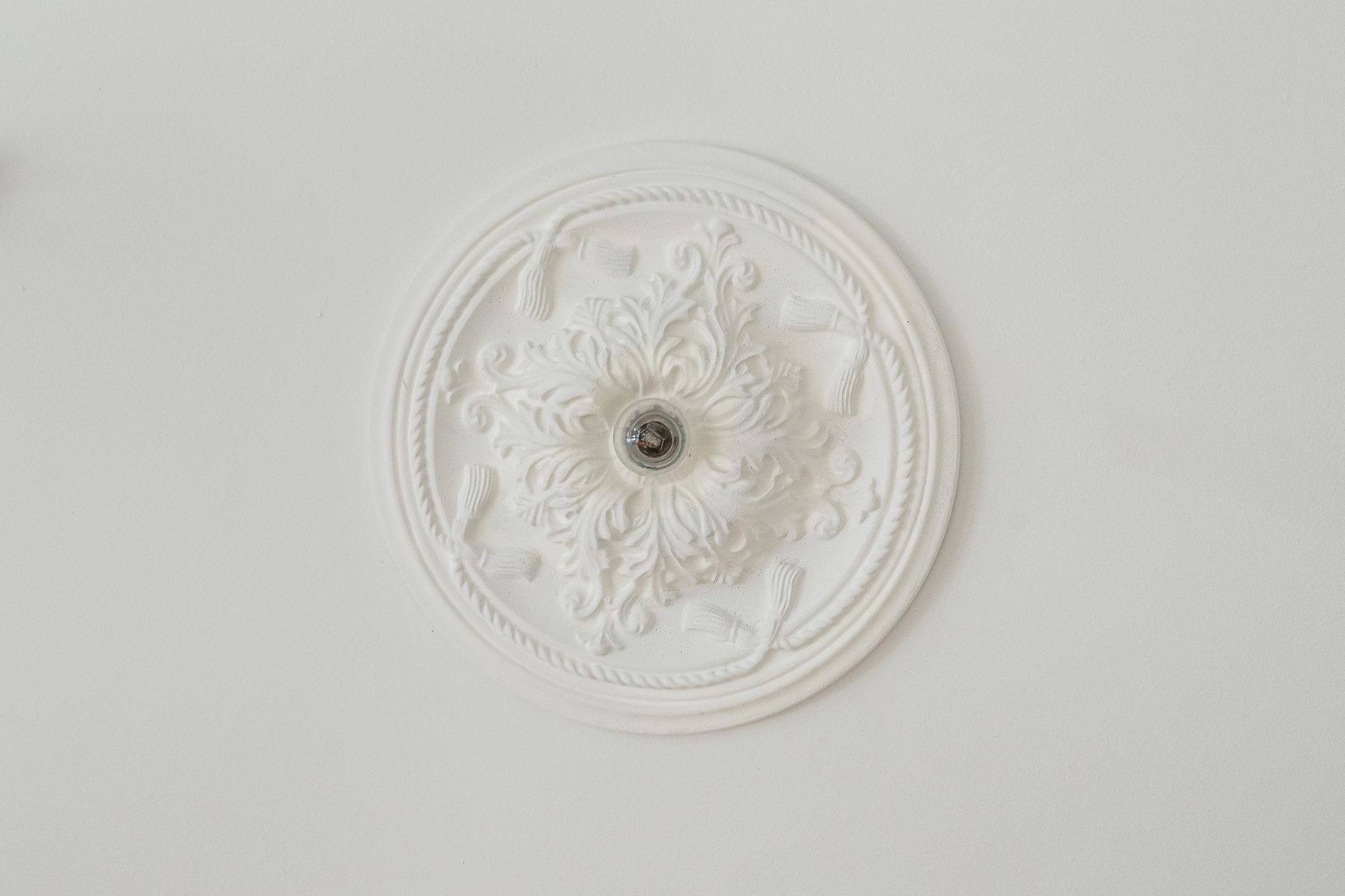 Weiße, verzierte Stuckrosette an einer Zimmerdecke mit Metallfassung in der Mitte.
