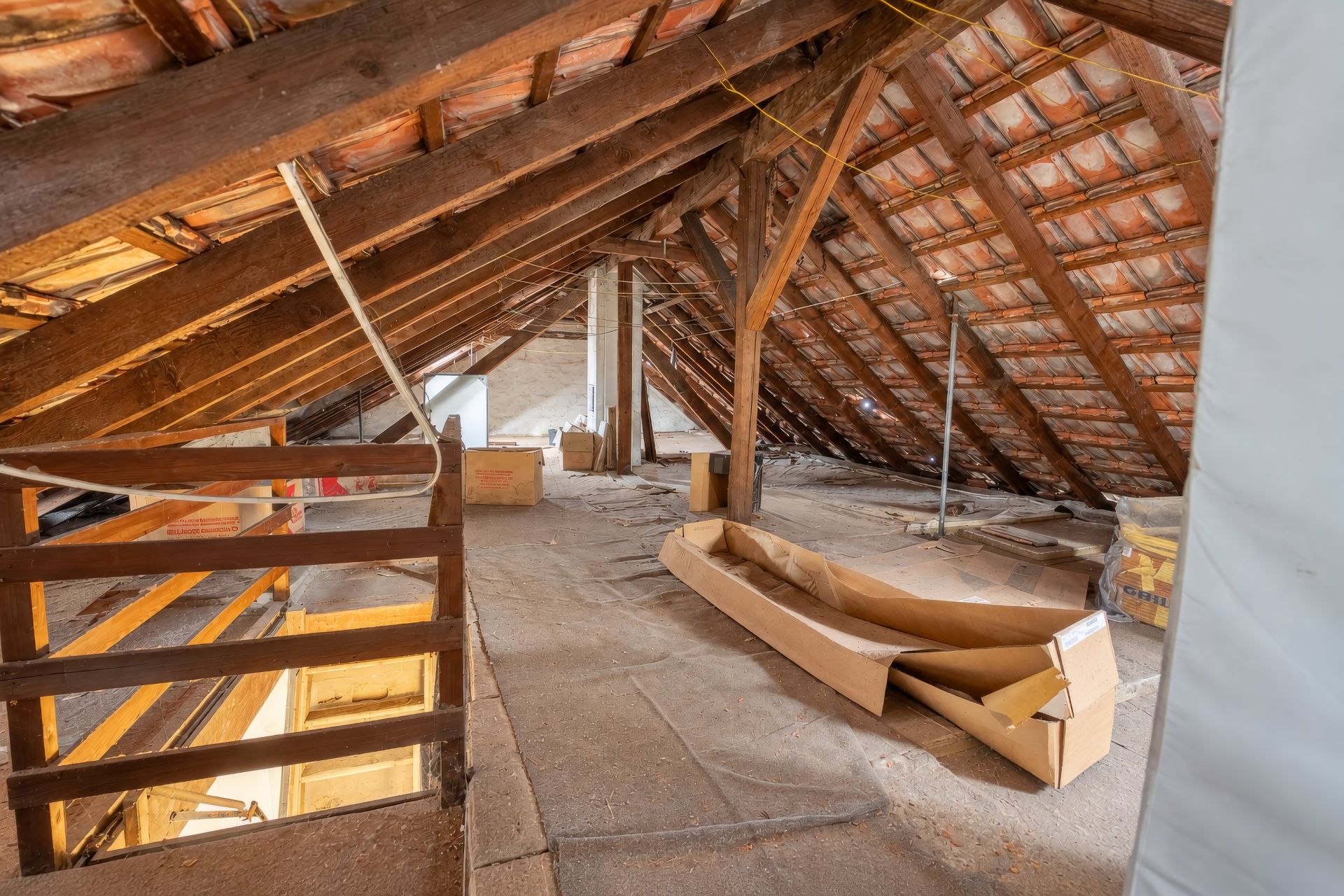 Dachboden mit sichtbaren Holzbalken, Kartons und offenem Dachstuhl.