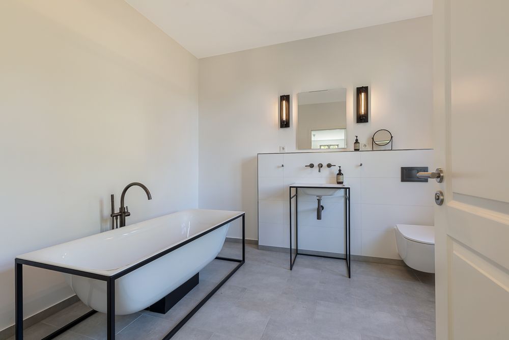 Modernes Badezimmer mit freistehender Badewanne, Waschbecken, Spiegel und Wandtoilette.
