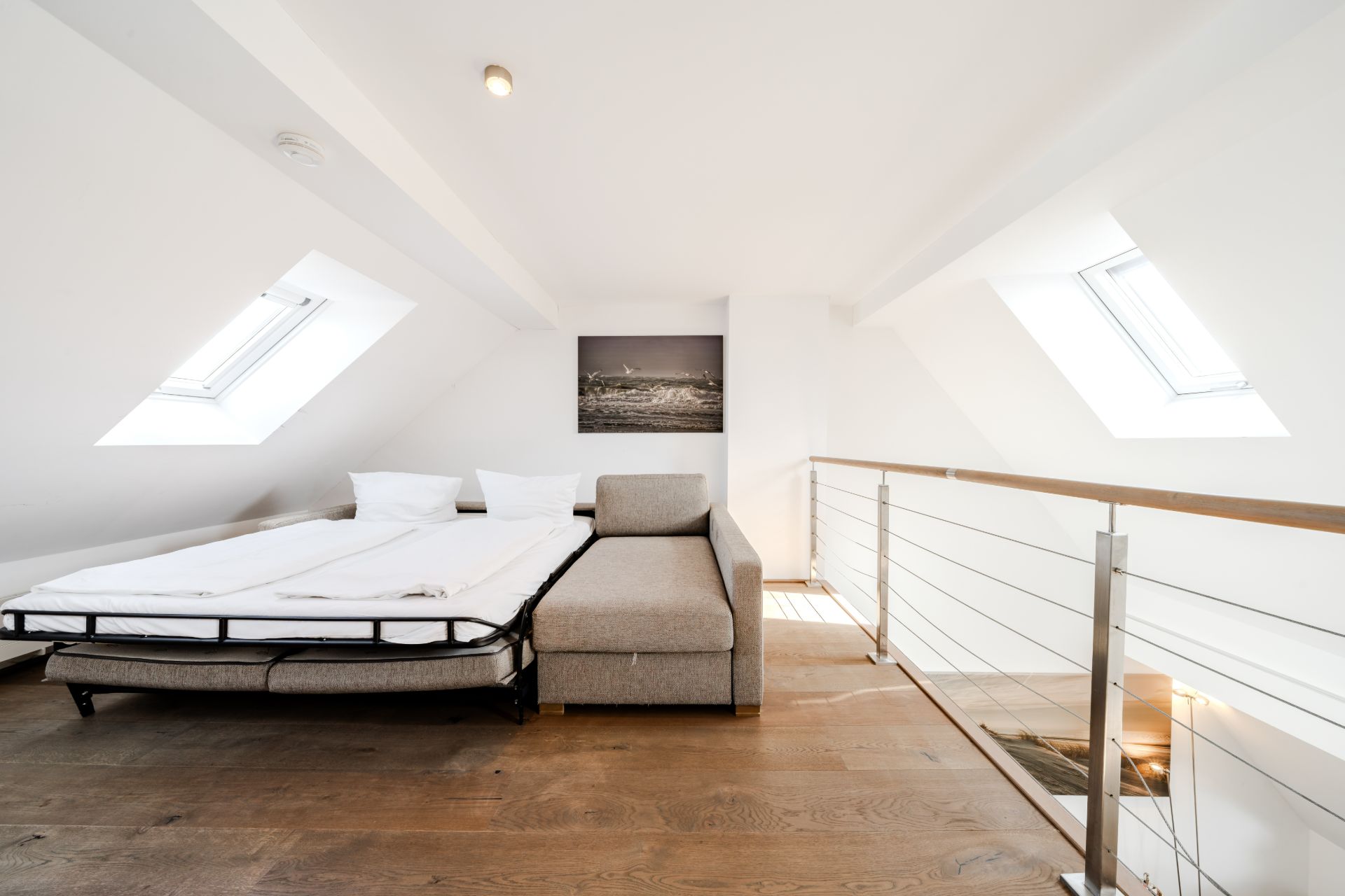 Helles Zimmer mit Schlafsofa, Holzfußboden und zwei Dachfenstern.