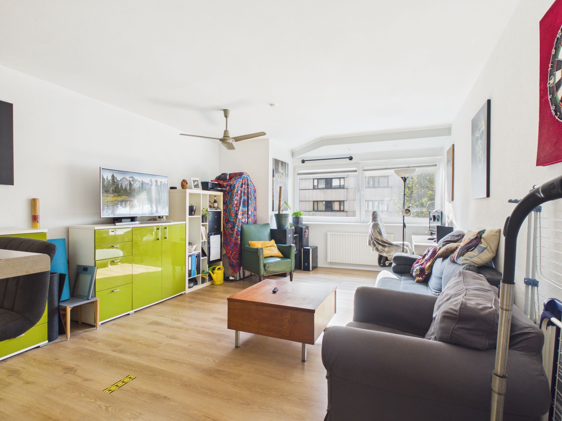 Helles Wohnzimmer mit Sofa, Couchtisch, grünem Schrank und großen Fenstern.