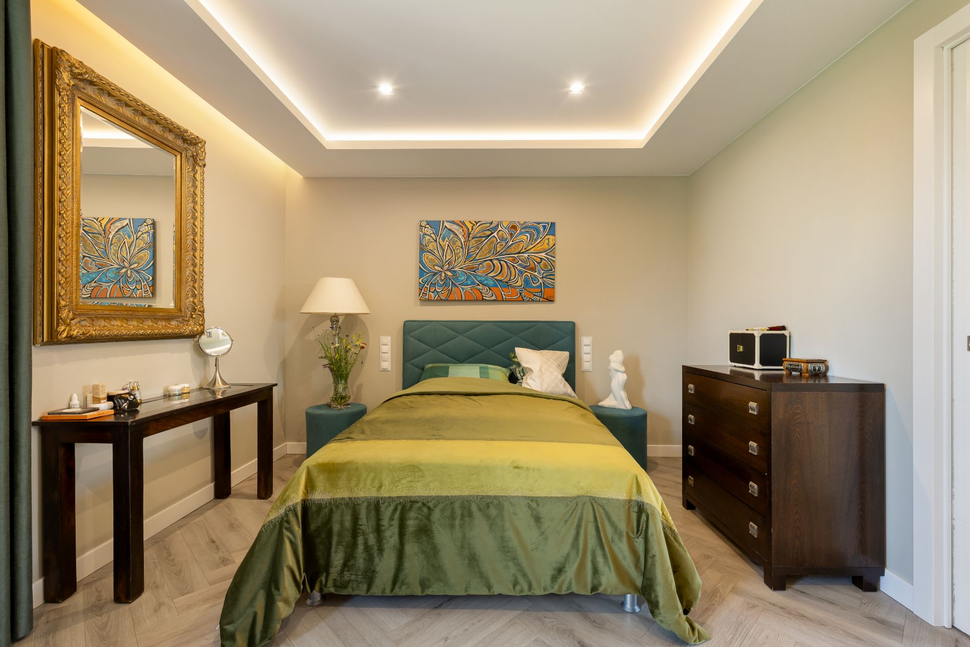 Schlafzimmer mit grünem Bett, Nachttischen, Kommode, Wandbild und großem Spiegel.