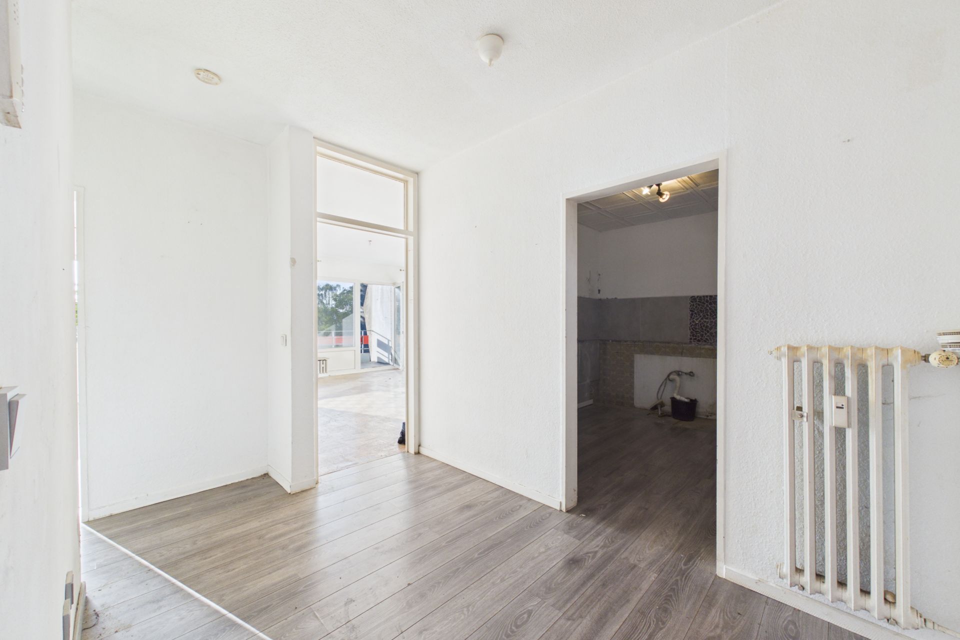 Heller Flur mit Holzboden, Tür zu einem weiteren Raum und großem Fenster.