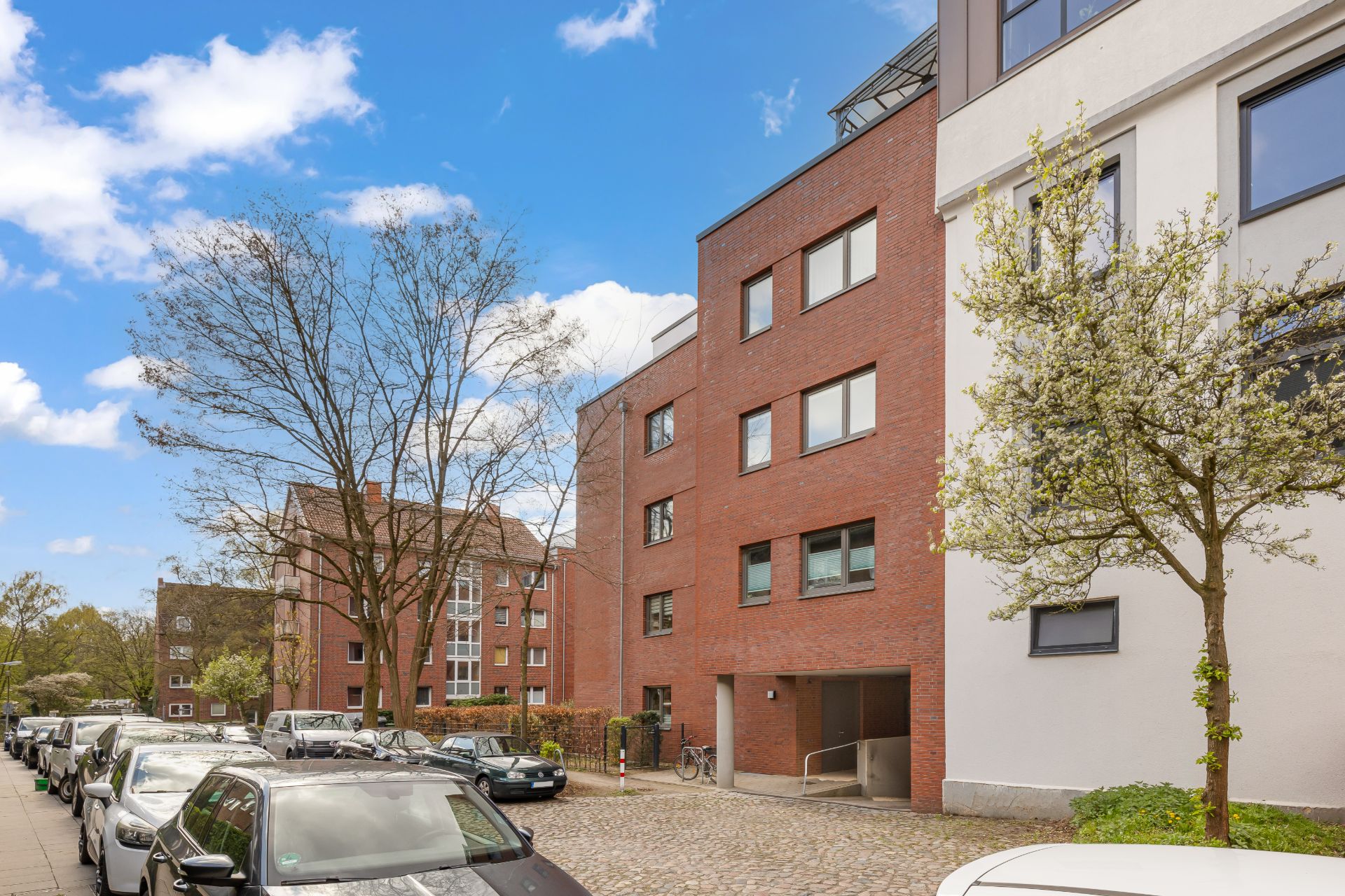 Moderne Wohngebäude mit roten und weißen Fassaden an einer Straße mit geparkten Autos und Bäumen.