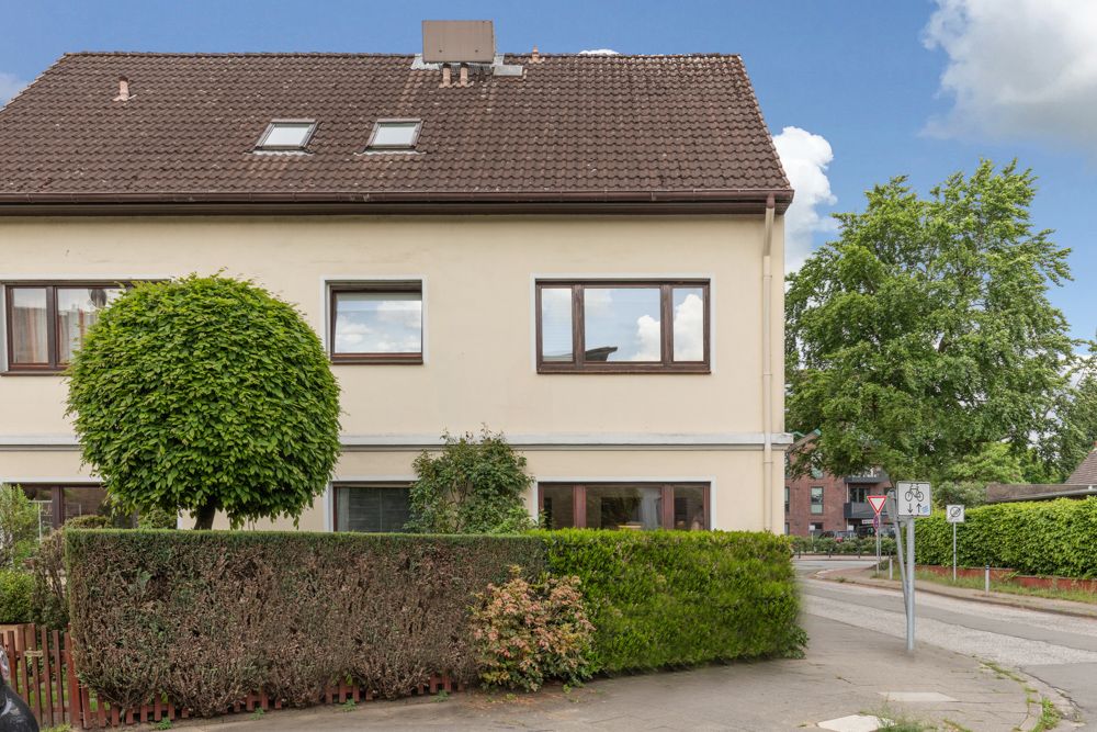 Doppelhaushälfte mit braunem Dach, großen Fenstern und Garten an einer Straßenecke.