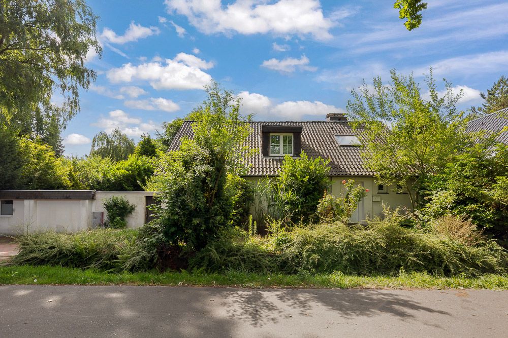 Wohnhaus mit schrägem Dach und viel bewachsener Vorgarten, von Bäumen und Sträuchern umgeben.